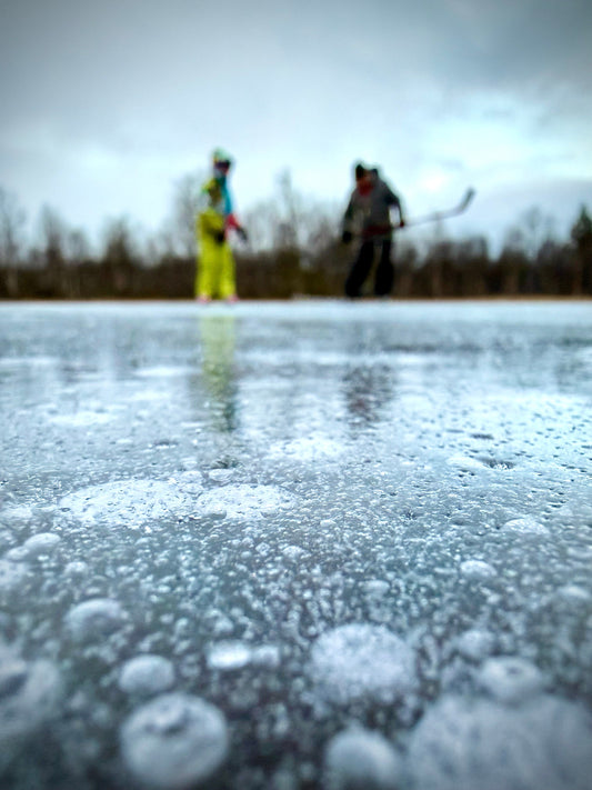 boy and father playing ice hockey on a frozen lake
